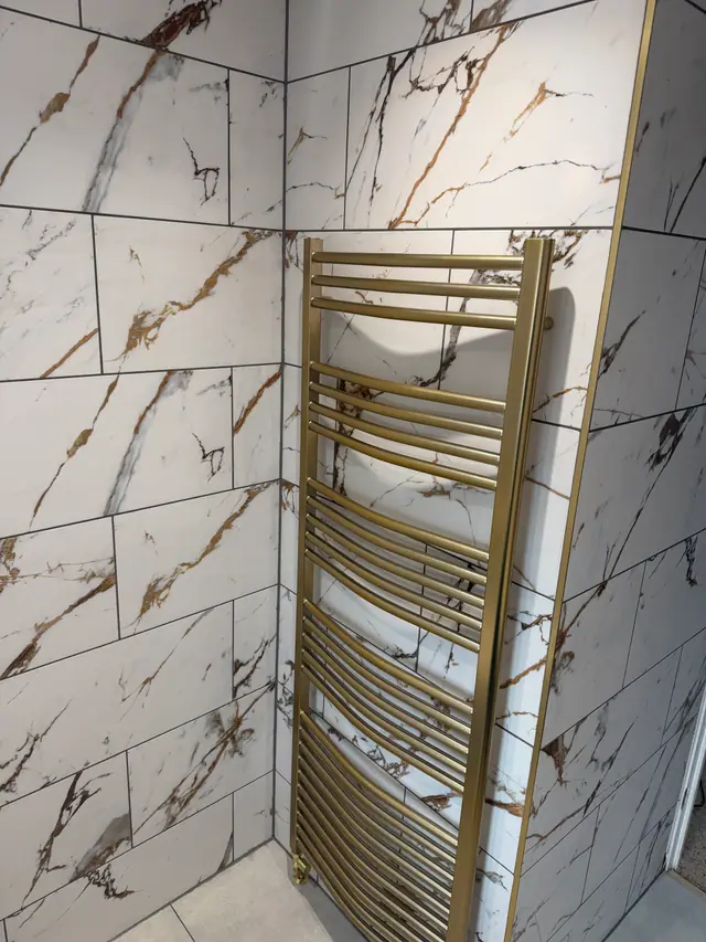 Brushed gold towel rail against precision-laid marble-effect tiles