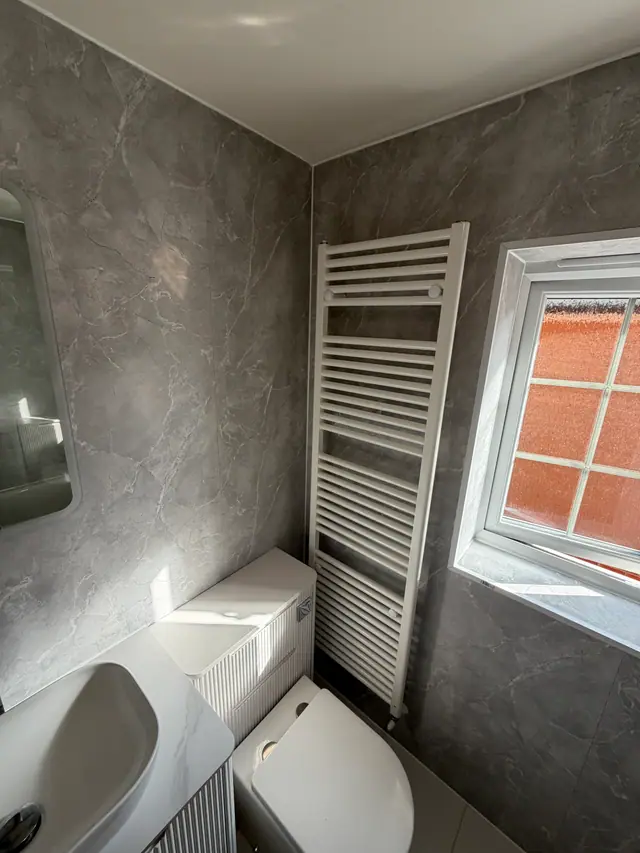 Tall white towel radiator set against grey wall panels