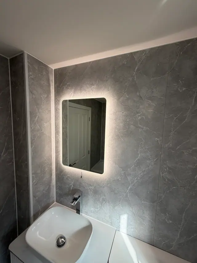 Illuminated mirror and countertop basin against grey wall panels
