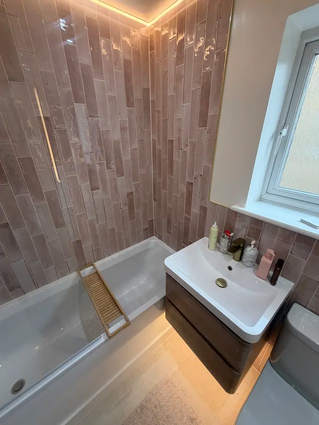 Finished bathroom with warm pink tiles, bath and floating vanity