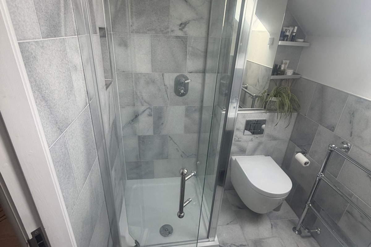 Completed grey-tiled bathroom with a walk-in shower, wall-hung toilet and chrome towel rail